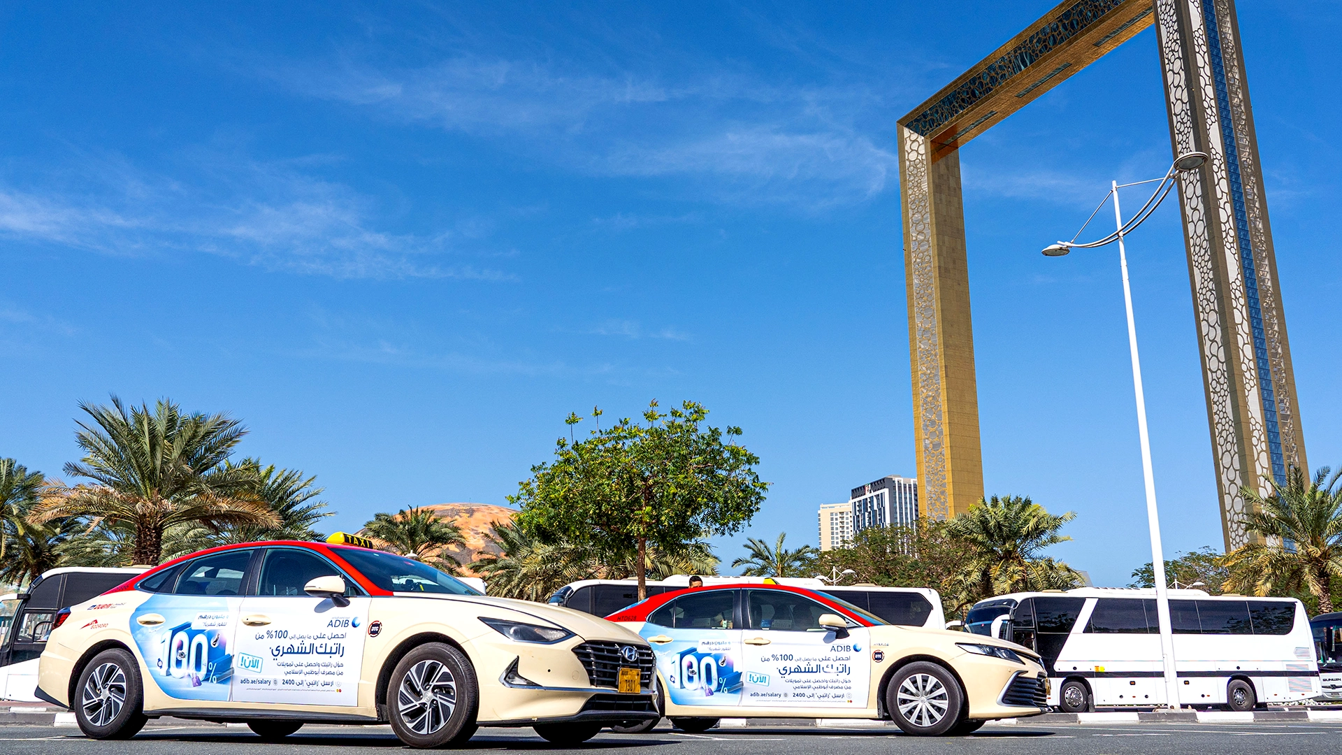 Taxis with adverts for ADIB wait underneath the Dubai Frame