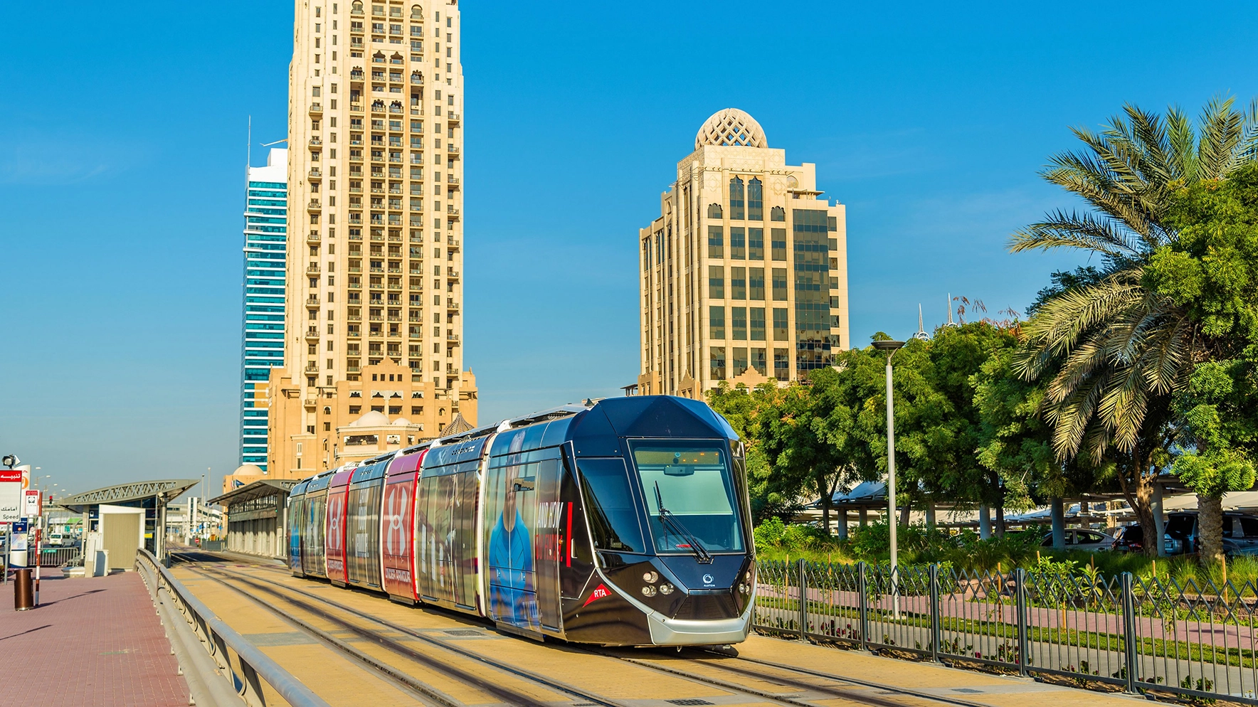 A tram branded for Under Armour passes by traditional architecture in Dubai Marina