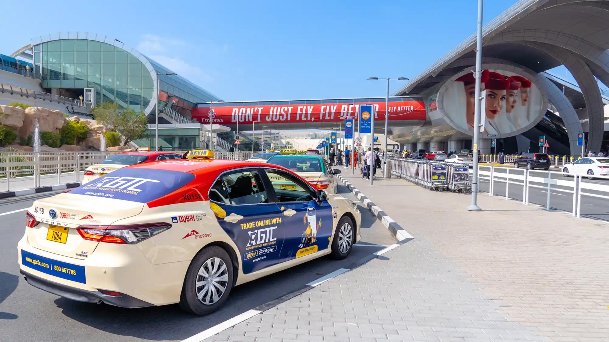 A taxi with bold advertising for GTC arrives at Dubai International Airport