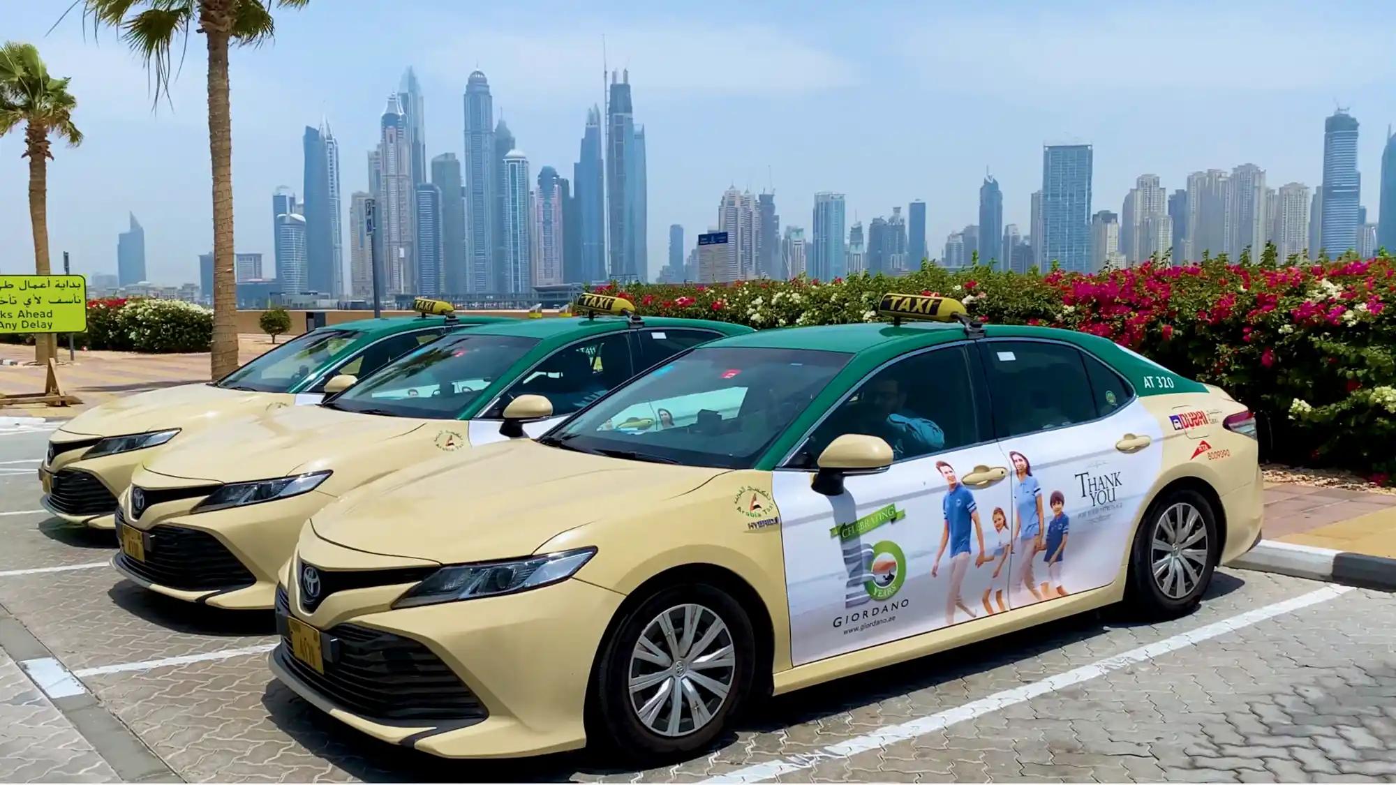 Taxis with adverts for ADIB wait underneath the Dubai Frame