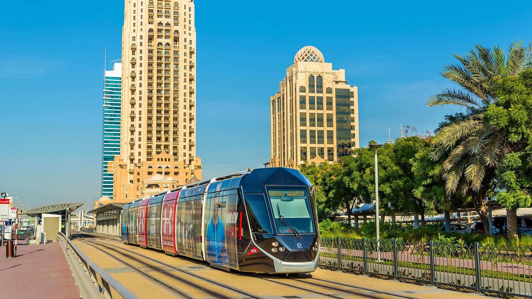 A tram branded for Under Armour passes by traditional architecture in Dubai Marina